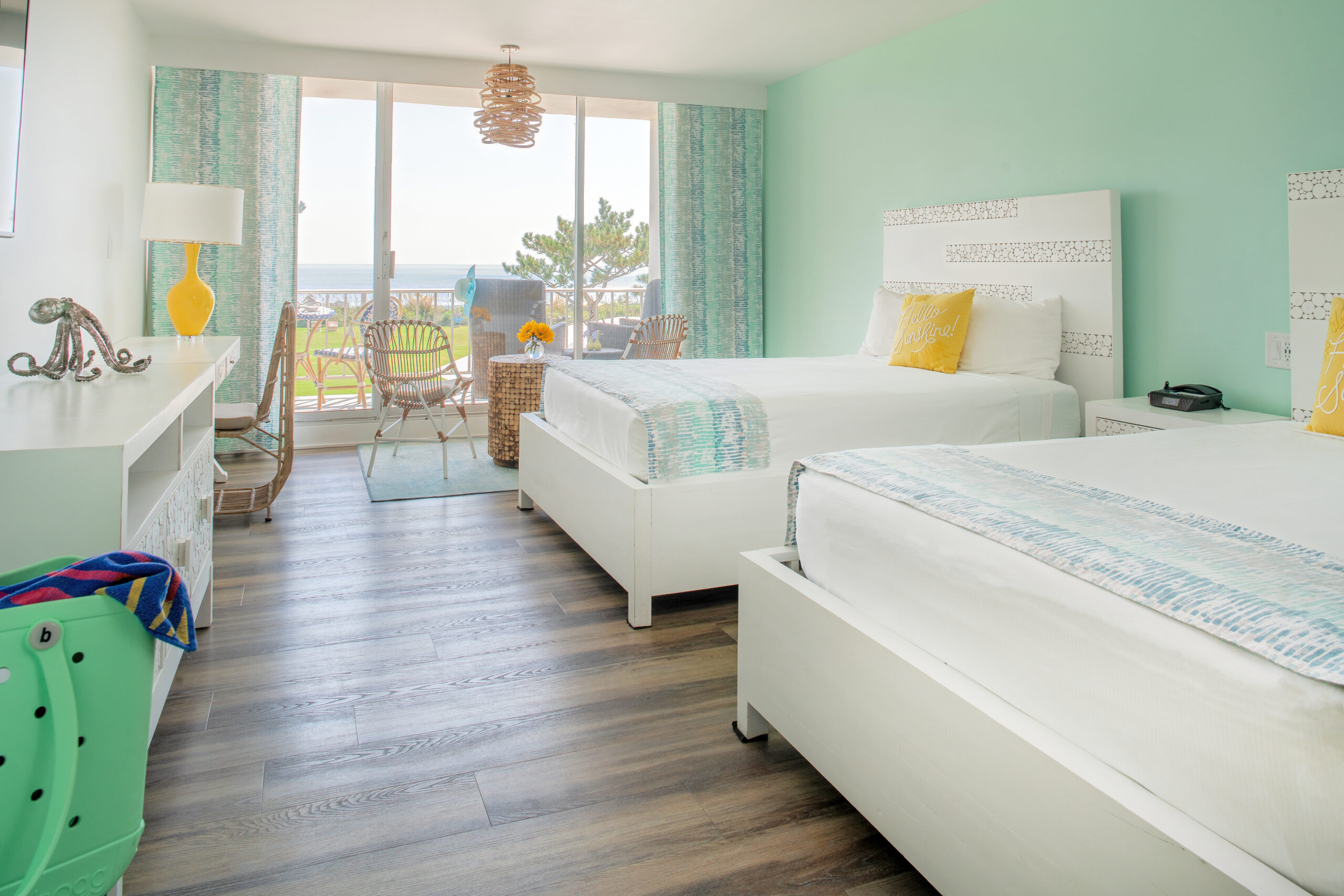 Brightly colored oceanfront guest room with two beds and patio seating area.