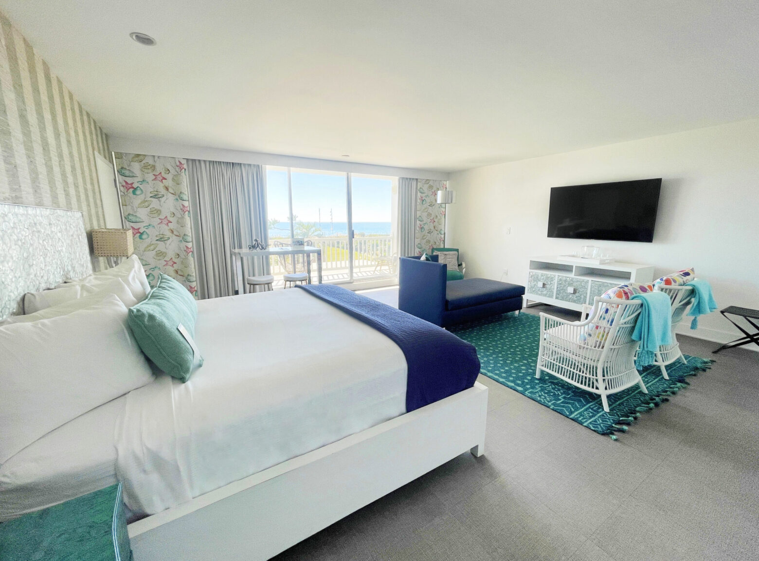 Colorful oceanfront stateroom with bed, seating and television.