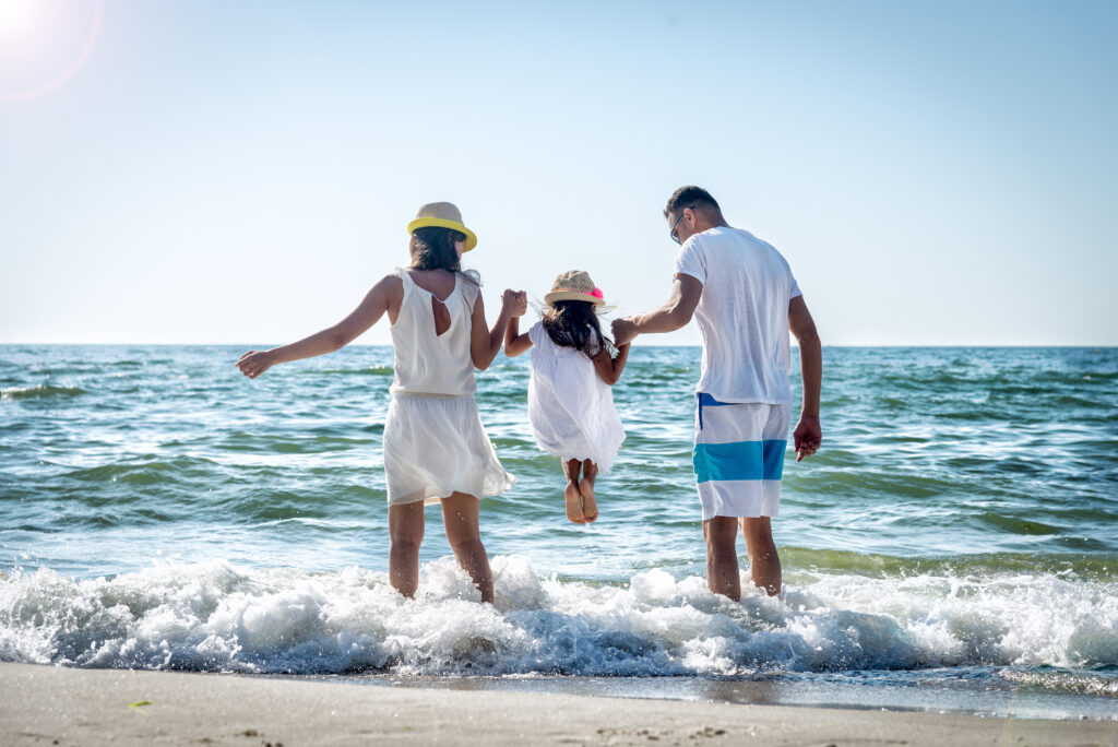 Family of three jumping in the waves at the beach.